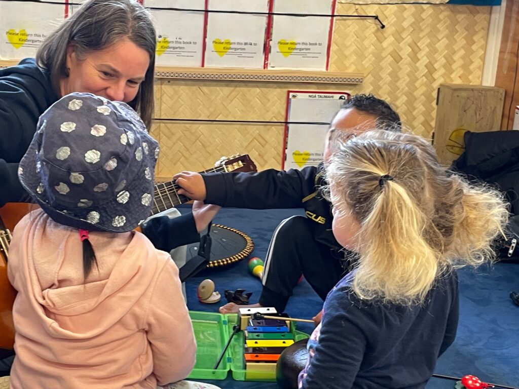 An image of a music therapy session with a person playing guitar with several young participants