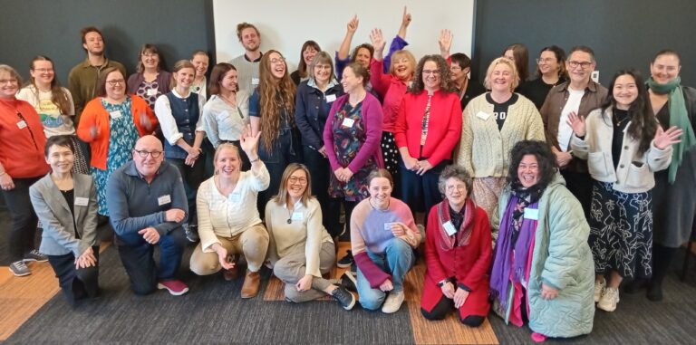 A group of people smiling at each other and some are smiling and waving towards the camera
